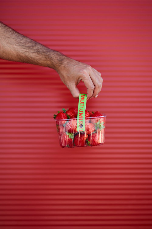 Fotografía en la que se ve una cesta de medio kilo de fresas de mumu en una pared de color corporativo.